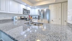 Una cocina moderna con encimeras de granito, electrodomésticos de acero inoxidable y muebles de cocina blancos.
