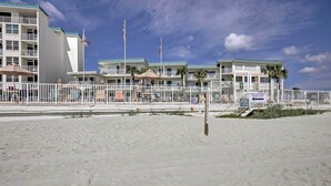 Un hotel frente a la playa con varios balcones, un área de playa cercada y un letrero que indica que los baños públicos están en el segundo piso.