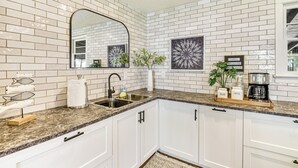 A kitchen with white cabinets, a granite countertop, a sink, and a coffee maker.
