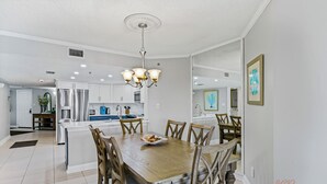 Une cuisine moderne avec des meubles blancs, un îlot central et un coin repas comprenant une table et des chaises en bois.