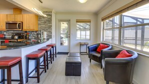 Cozinha moderna com ilha central, banquetas e área de estar com sofá e cadeiras.