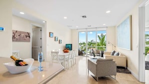 A modern living room with a dining area, a sofa, and a balcony with a view. - Hemingway Condo - Sunset View & steps to the beach (Deerfield Beach)