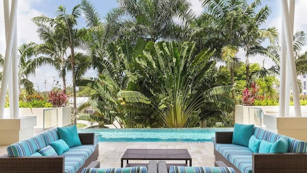 A poolside area with wicker furniture and a view of a large palm tree. - Hemingway Condo - Sunset View & steps to the beach (Deerfield Beach)