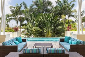 A poolside area with wicker furniture and a view of a large palm tree.