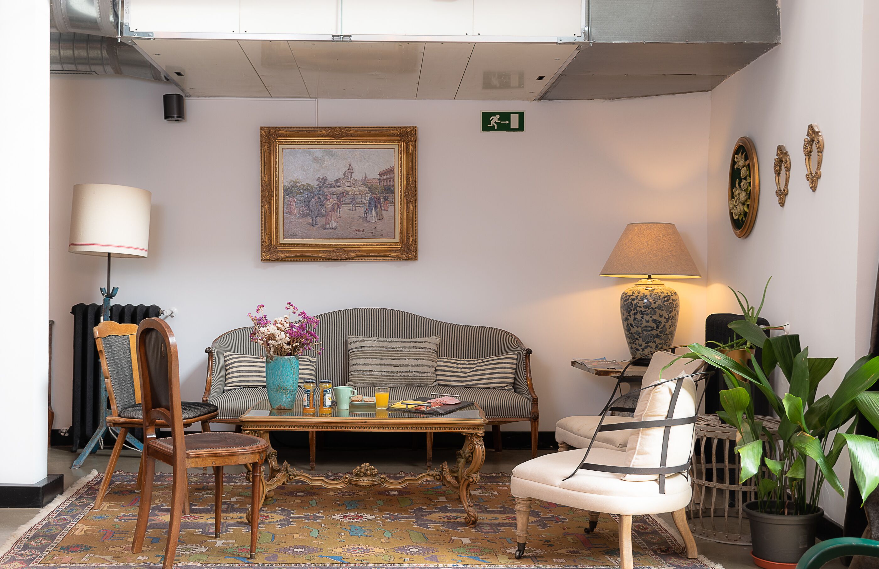 Ein gemütliches Wohnzimmer mit einem gestreiften Sofa, einem Holzstuhl, einem Couchtisch mit Büchern und einer Vase sowie einer Topfpflanze.