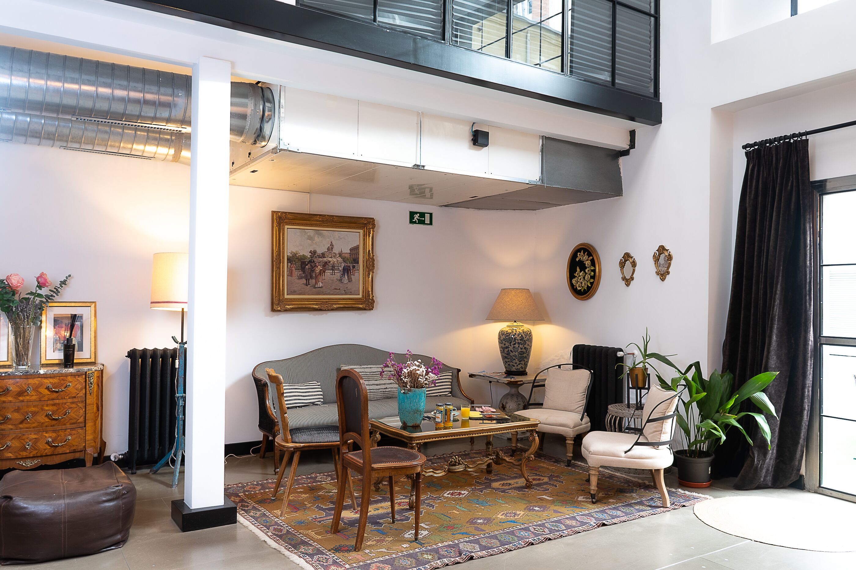 A spacious living room with a high ceiling, a sofa, chairs, a coffee table, and a large window with curtains.