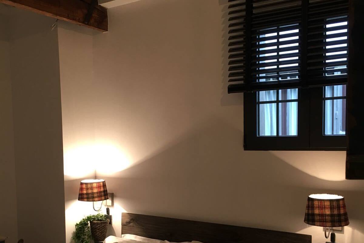 Quarto com cabeceira de madeira, duas luminárias de cabeceira, janela com persianas e cama com almofadas estampadas.