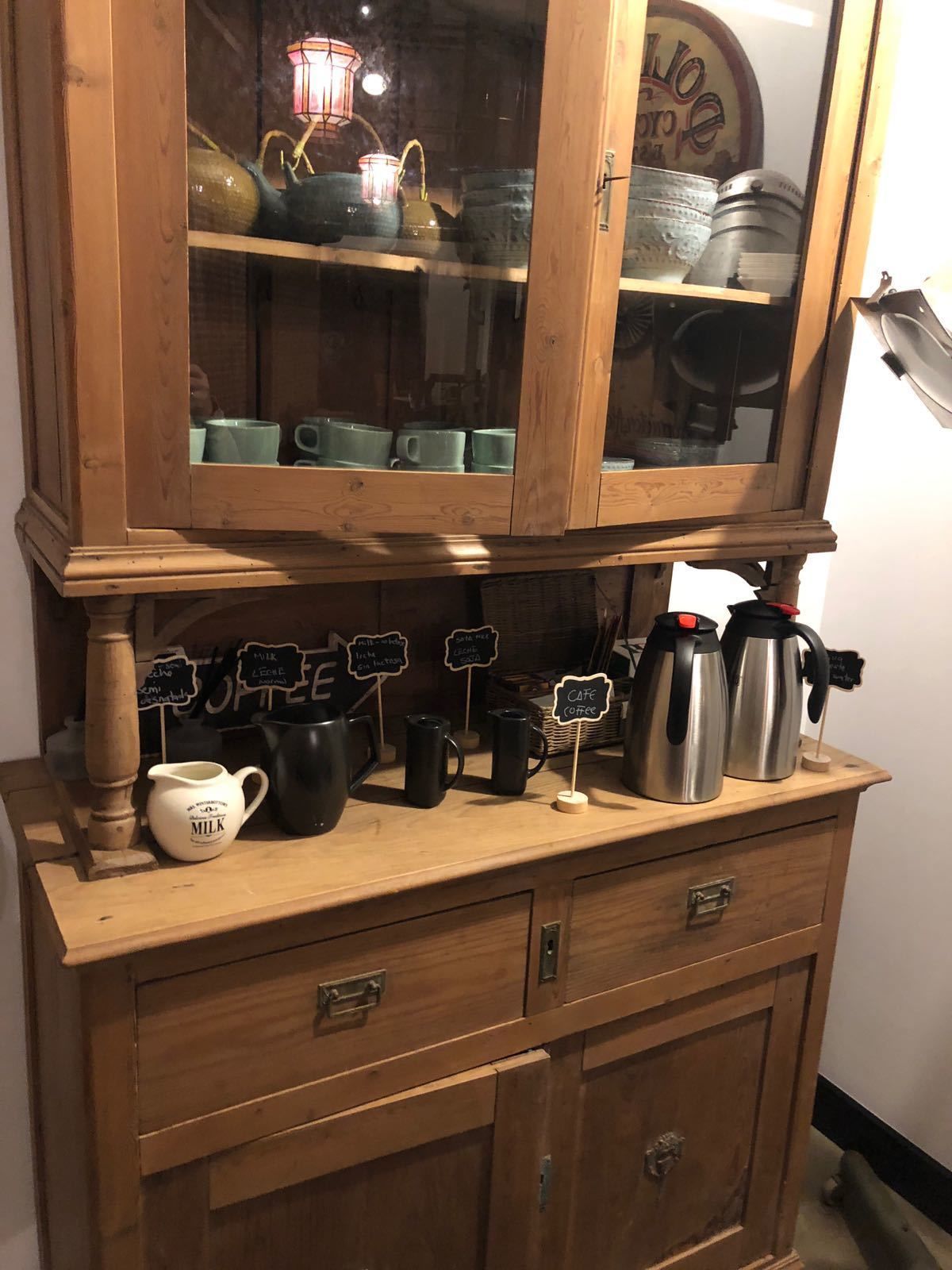 Un meuble en bois doté de portes en verre, contenant divers ustensiles de cuisine, comme des tasses et un pot à lait.