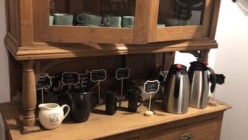 A wooden cabinet with glass doors, containing various kitchen items like mugs and a milk jug.