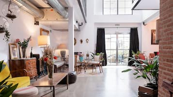 Relax in this stylish space with a sofa, dining table, and bench, surrounded by artwork and lush greenery.