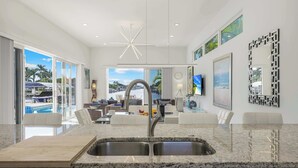 Een moderne keuken met een groot eiland, een inbouwspoelbak en uitzicht op het zwembad en het terras.