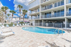 A hotel with a swimming pool, multiple balconies, and palm trees.