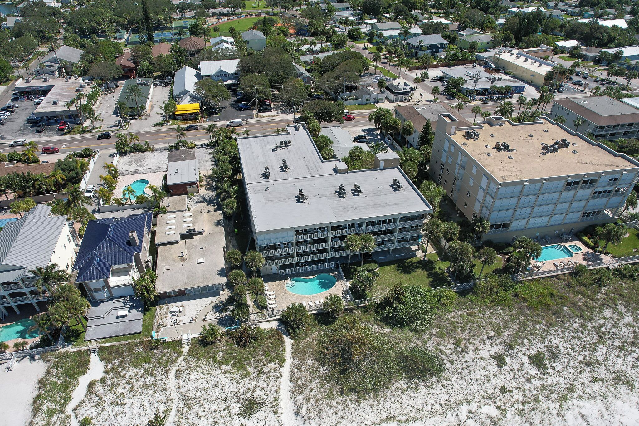 An aerial view of a coastal hotel with multiple buildings, a swimming pool, and surrounding greenery.