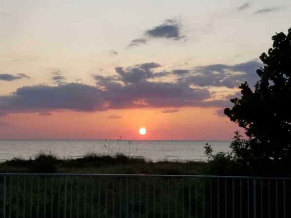 A sunset over the ocean with a metal railing in the foreground.