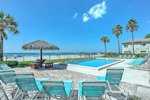 A pool area with lounge chairs, a thatched umbrella, and a view of the ocean.