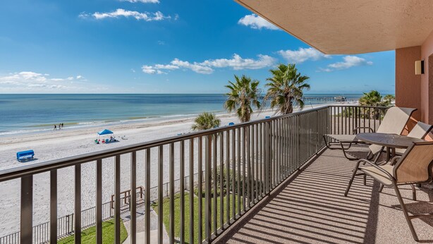 A balcony with a view of the beach, palm trees, and a clear sky.