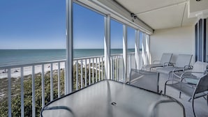 Un balcón con vista a la playa y al océano. Hay varias sillas y una mesa.