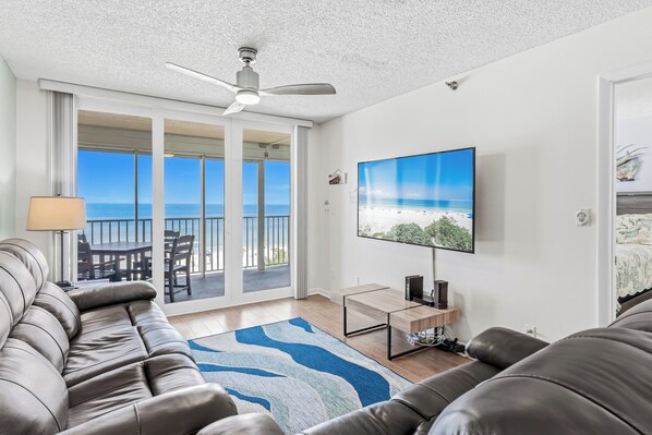 Una sala de estar moderna con un sofá de cuero, un televisor de pantalla plana montado en la pared y un balcón con vistas al océano.