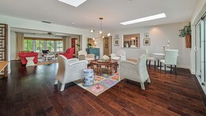 Ein geräumiges Wohnzimmer mit großem Fenster, einem roten Sofa, Korbstühlen, einem Couchtisch und einer dekorativen Vase.