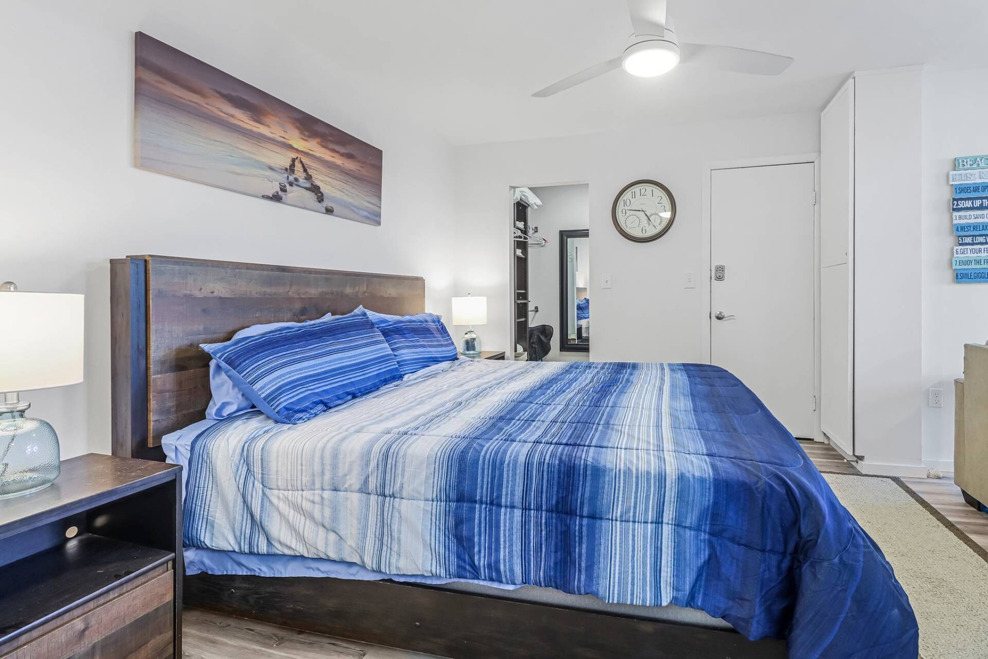 Ein Schlafzimmer mit Bett, Nachttisch, Deckenventilator, einer Uhr und einer Tür.