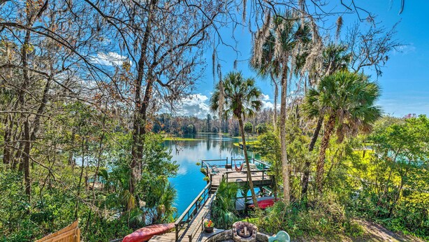 Une terrasse en bois avec un foyer, des sièges d’extérieur et une vue sur un lac entouré d’arbres.