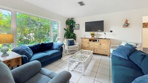 Un salon avec un canapé bleu, une table basse blanche et un téléviseur fixé au mur.