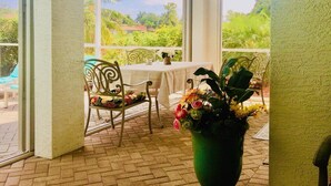 Un patio couvert avec une table et des chaises, une plante en pot et une vue sur la verdure environnante.