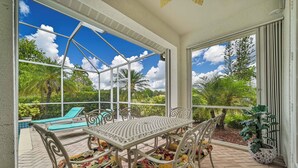 Une terrasse couverte avec une table et des chaises, une piscine et une vue sur la verdure.