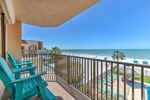 Un balcón con sillas Adirondack color turquesa, un área de piscina con sillones de descanso y vista a la playa y al océano.