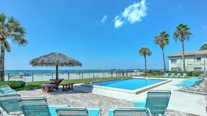 A pool area with lounge chairs, a thatched umbrella, and a view of the ocean.