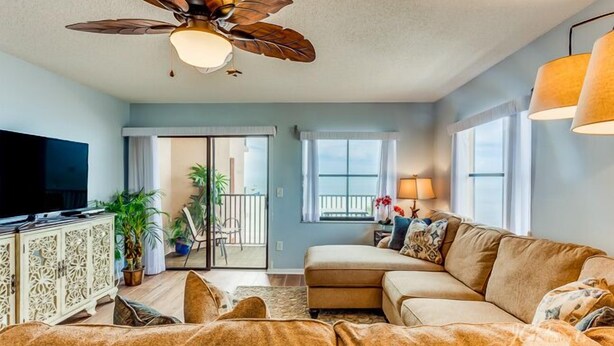 A living room with a sofa, a television, a ceiling fan, and a sliding glass door leading to a balcony.