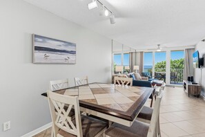 A modern living room with a dining area, large windows, and a view of the sea.