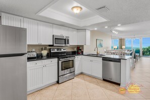 A modern kitchen with white cabinetry, stainless steel appliances, and a large island with a dishwasher.