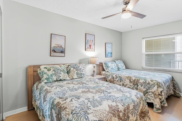 A bedroom with two beds, a ceiling fan, and a window with blinds.