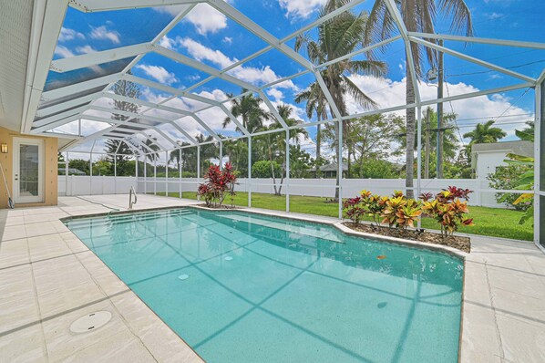 A swimming pool with a glass ceiling, surrounded by tropical plants and palm trees.