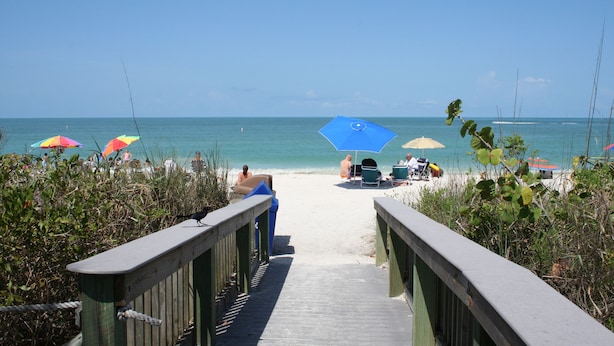 A wooden boardwalk leading to a beach with colorful umbrellas and lounge chairs.