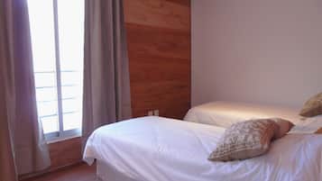 A bedroom with two beds, wooden paneling on the wall, and a window with curtains.