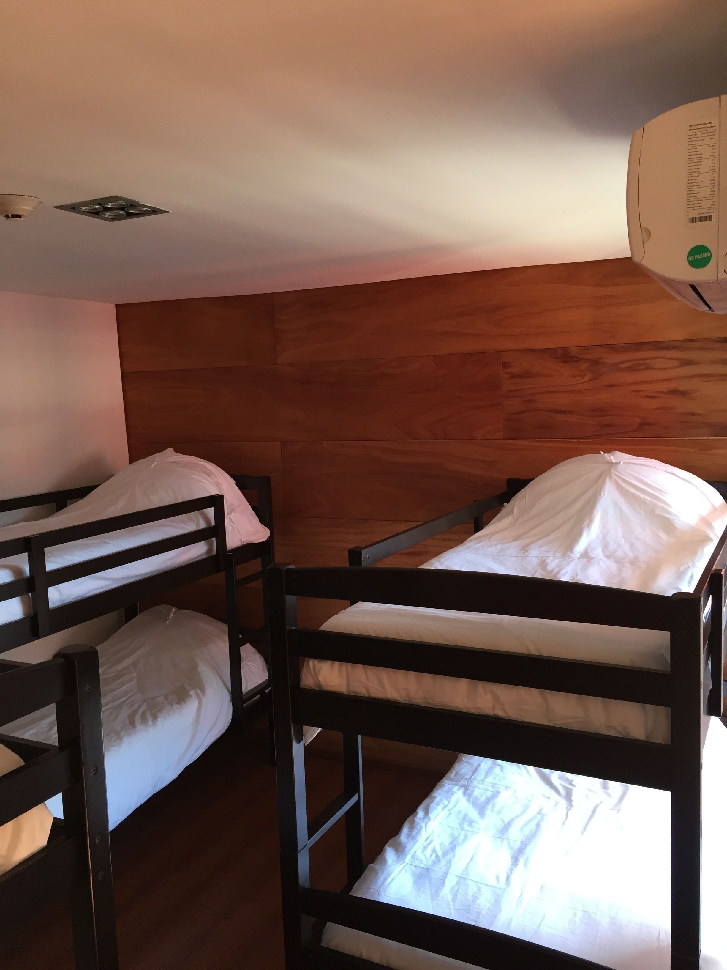 A room with bunk beds, wooden headboard, and a ceiling-mounted air conditioner.