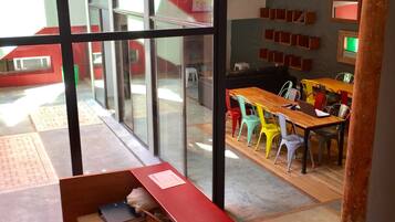 Un interior moderno con un separador de vidrio, un mostrador de recepción de madera y una zona de comedor con sillas de colores.