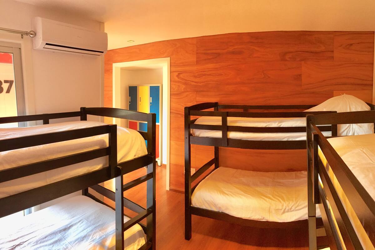 A room with bunk beds, wooden flooring, and a door with a colorful cabinet.
