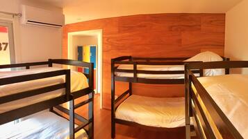 A room with bunk beds, wooden flooring, and a door with a colorful cabinet.