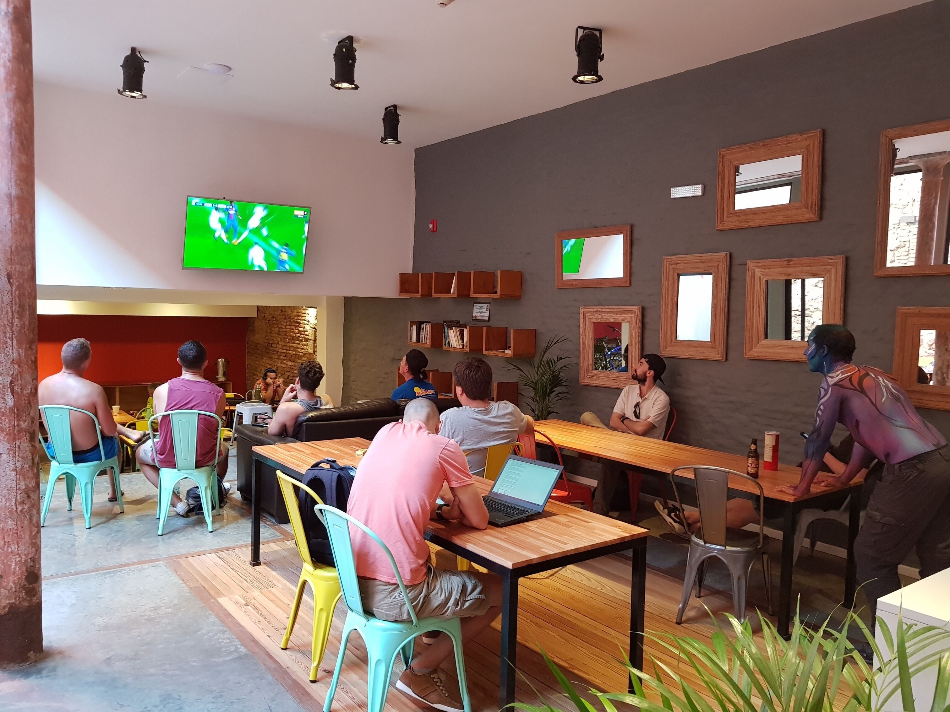 Un espacio interior moderno con varias zonas de estar, incluidas mesas y sillas, y un televisor de pantalla plana grande montado en la pared.