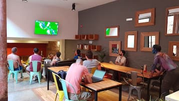 Un espacio interior moderno con varias zonas de estar, incluidas mesas y sillas, y un televisor de pantalla plana grande montado en la pared.