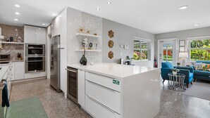Een moderne keuken met inbouwapparatuur, een centraal eiland en een eethoek met een blauwe bank en een kleine tafel.