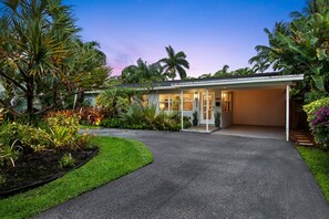 A modern house with a covered driveway, surrounded by lush tropical vegetation. - Experience Casa del Sol: A Midcentury Tropical Getaway with Classic South Florida Vibes! (Wilton Manors)