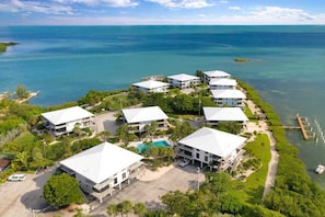 Um resort com vários edifícios de telhado branco, uma piscina e um cais que se estende sobre a água.