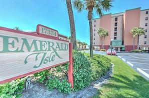 A wooden sign for Emerald Isle with a building in the background. - Emerald Isle 203 is a Gold 3-bedroom 2 bath Direct Gulf Front Condo. (N. Redington Beach)