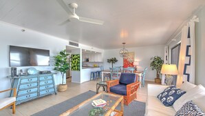 Un salón amplio con sofá, sillón y mesa de centro. Se ve una cocina al fondo.