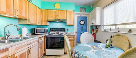 A compact kitchen with wooden cabinets, a microwave, stove, and a dining area with a table and chairs.