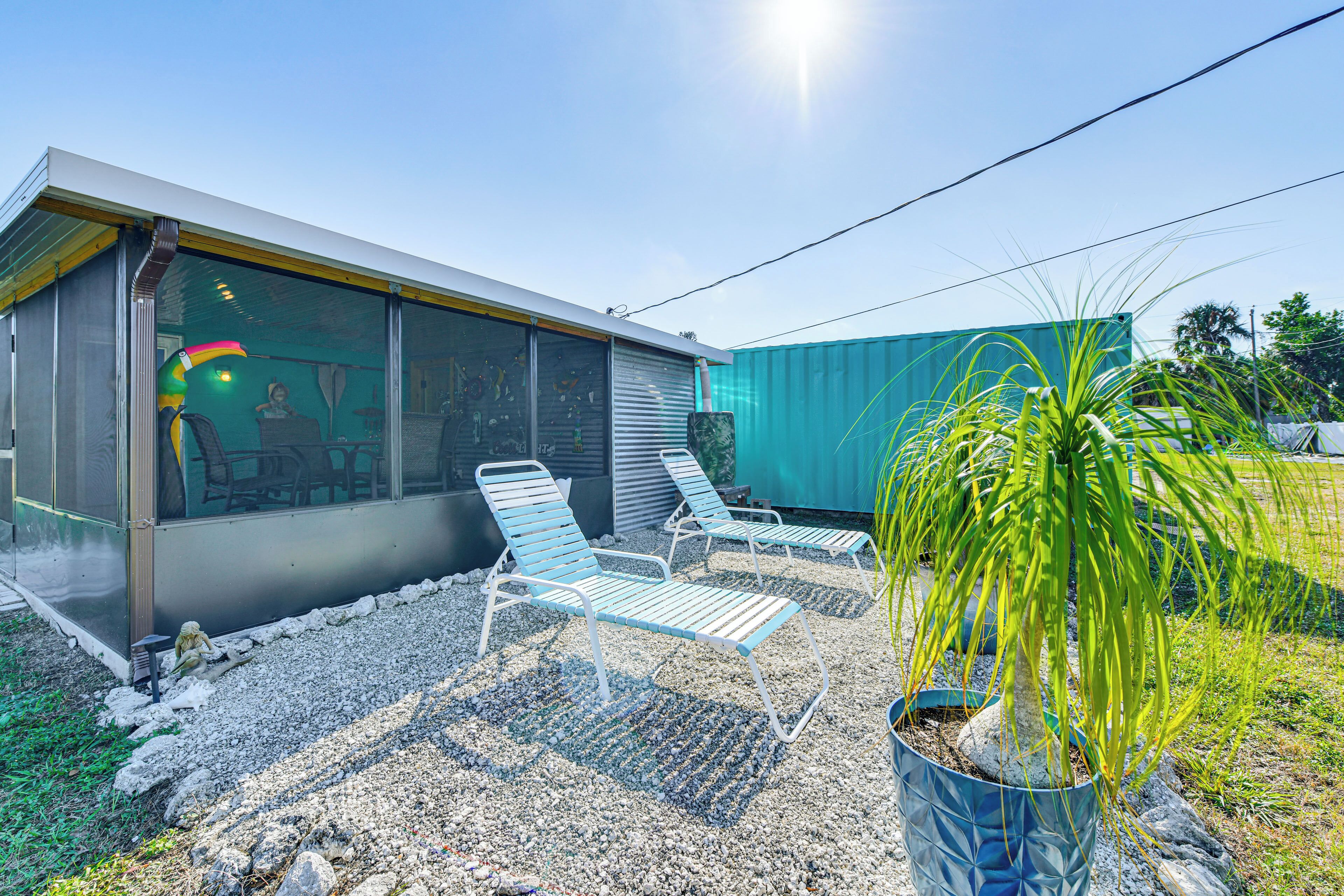 A modern building with large windows and a covered outdoor area with two lounge chairs and a potted plant.